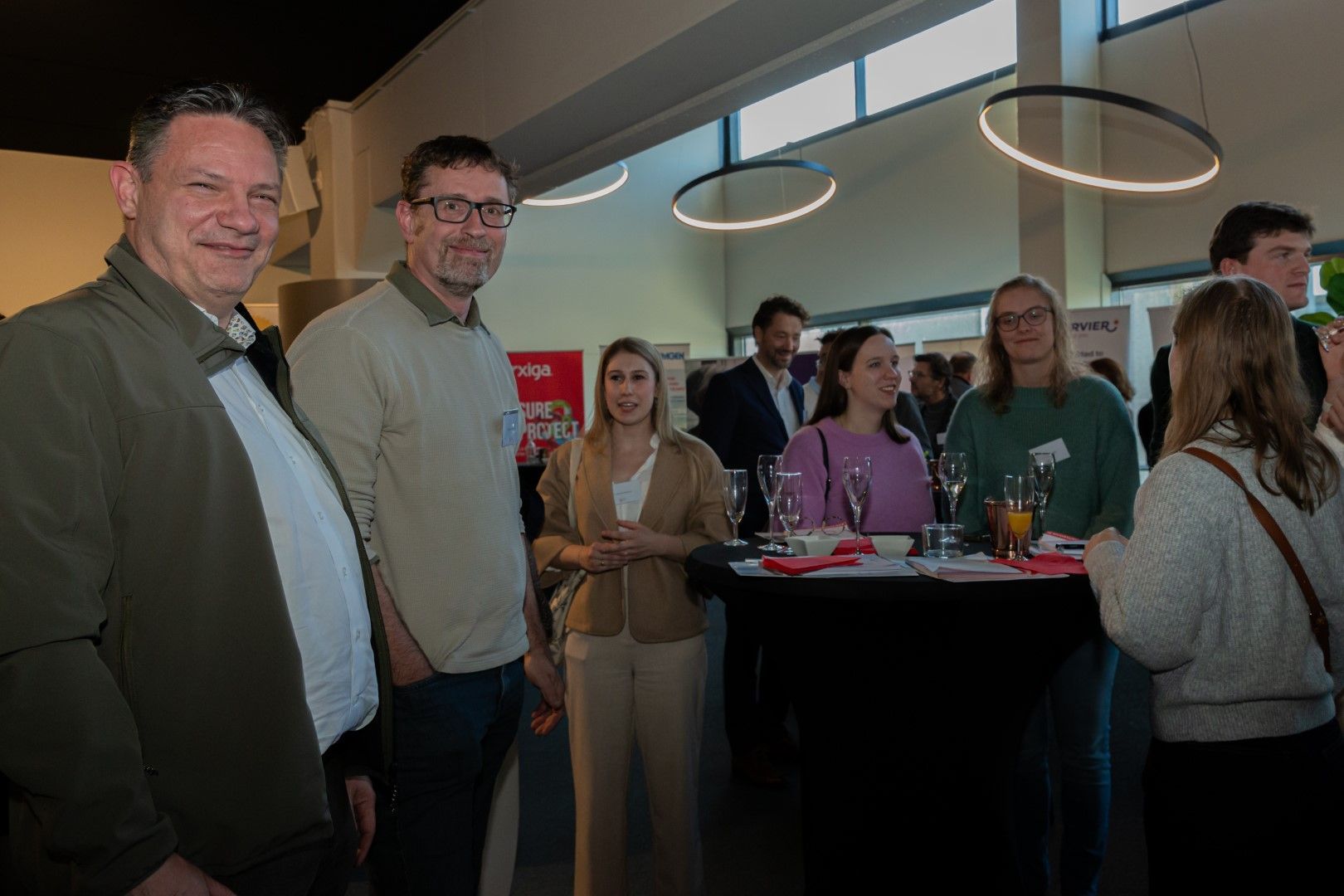 Mensen die met elkaar in gesprek zijn tijdens een netwerkevenement rond een hoge tafel in een moderne kantoorruimte.