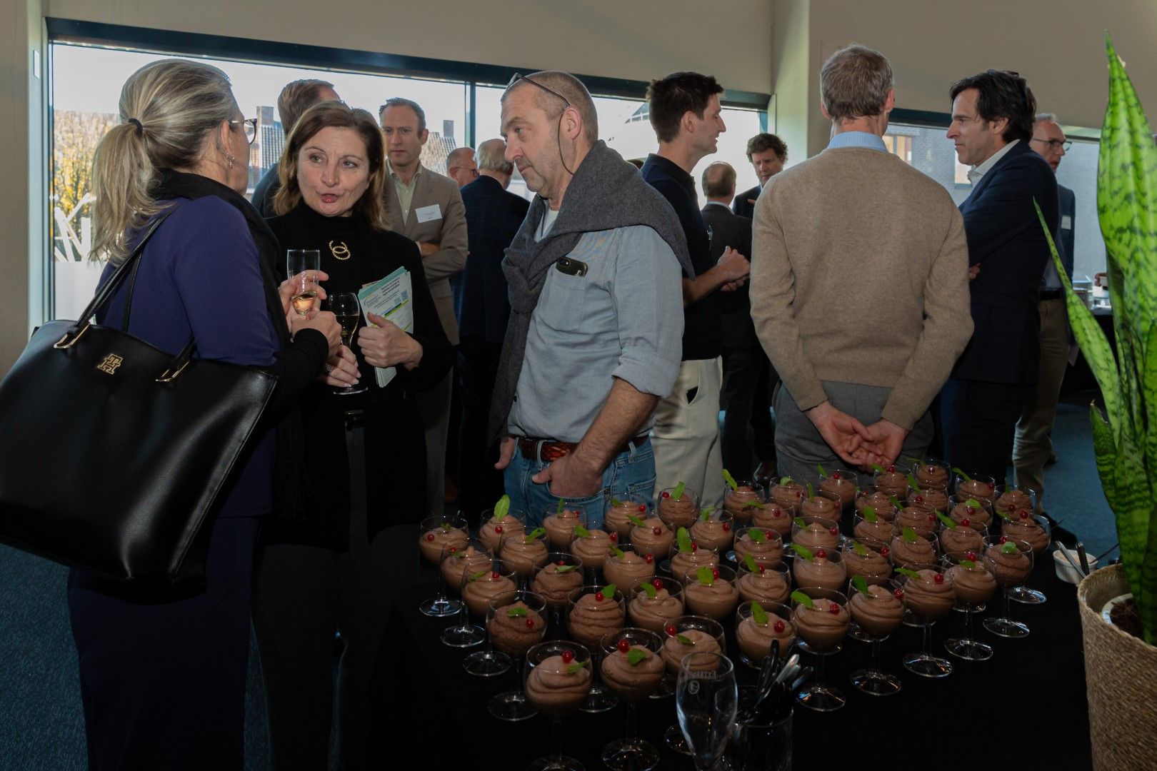 Gasten mengen zich onder elkaar tijdens een evenement binnenshuis, naast een tafel vol cupcakes.