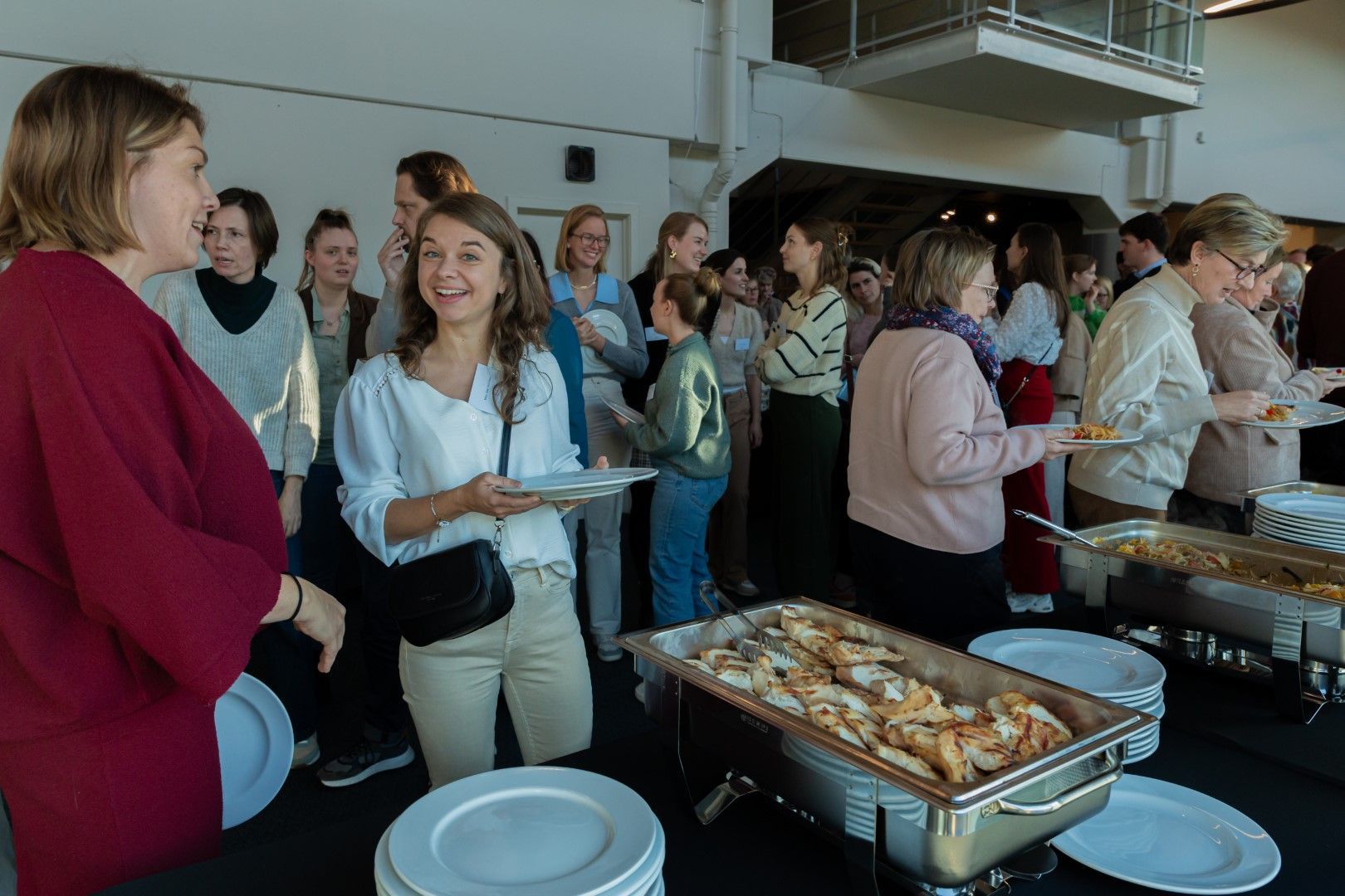 Mensen staan bij een buffettafel op een evenement binnenshuis en scheppen zelf eten en drinken op.