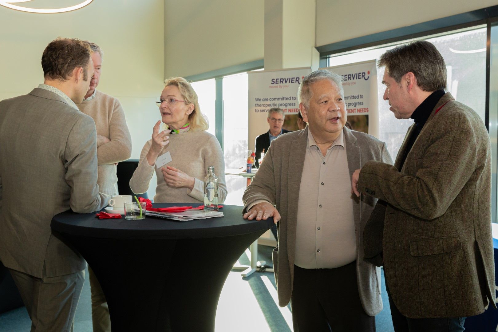Mensen die met elkaar praten aan een staande tafel in een lichte vergader- of netwerkruimte.
