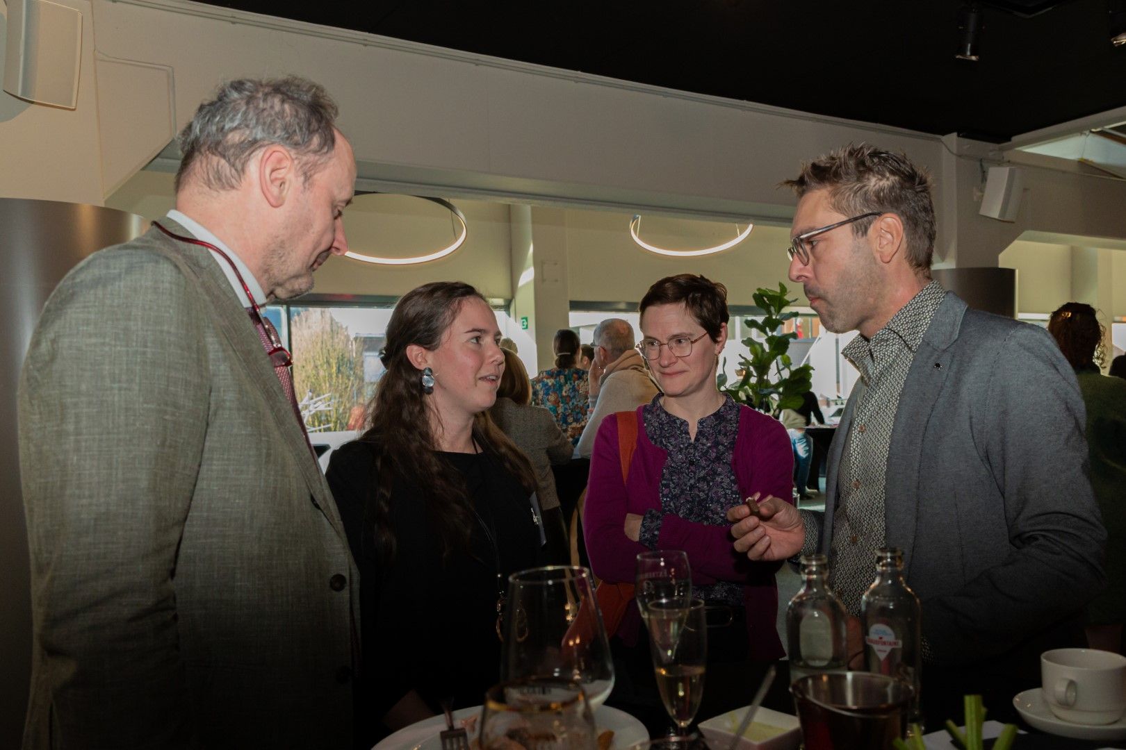 Vier mensen zitten te praten aan een bar, met drankjes en flessen op tafel.