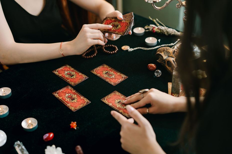 Hands dealing tarot cards on a black table with candles and crystals