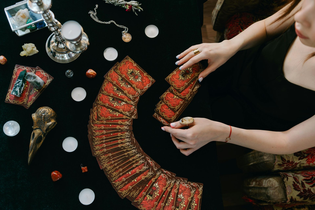Hands arranging a red and gold beaded necklace on a black surface with jewelry tools and ornaments