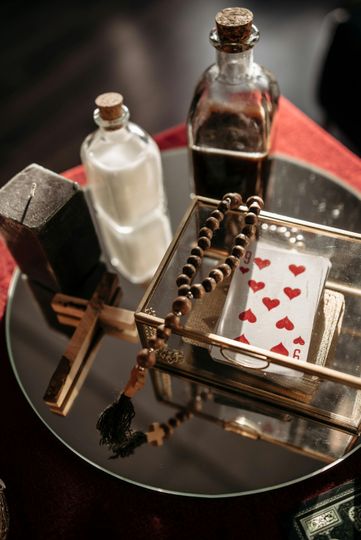 Small tabletop altar with bottles, a cross, and red heart decorations on a round tray