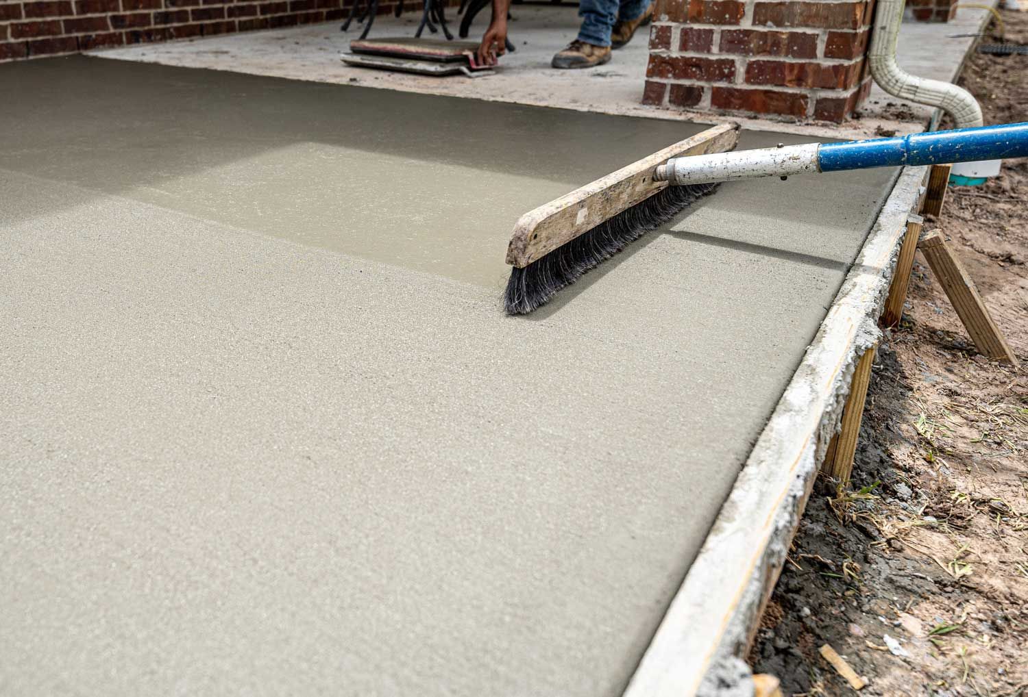 Fresh concrete being smoothed with a trowel beside a brick wall and sidewalk edge