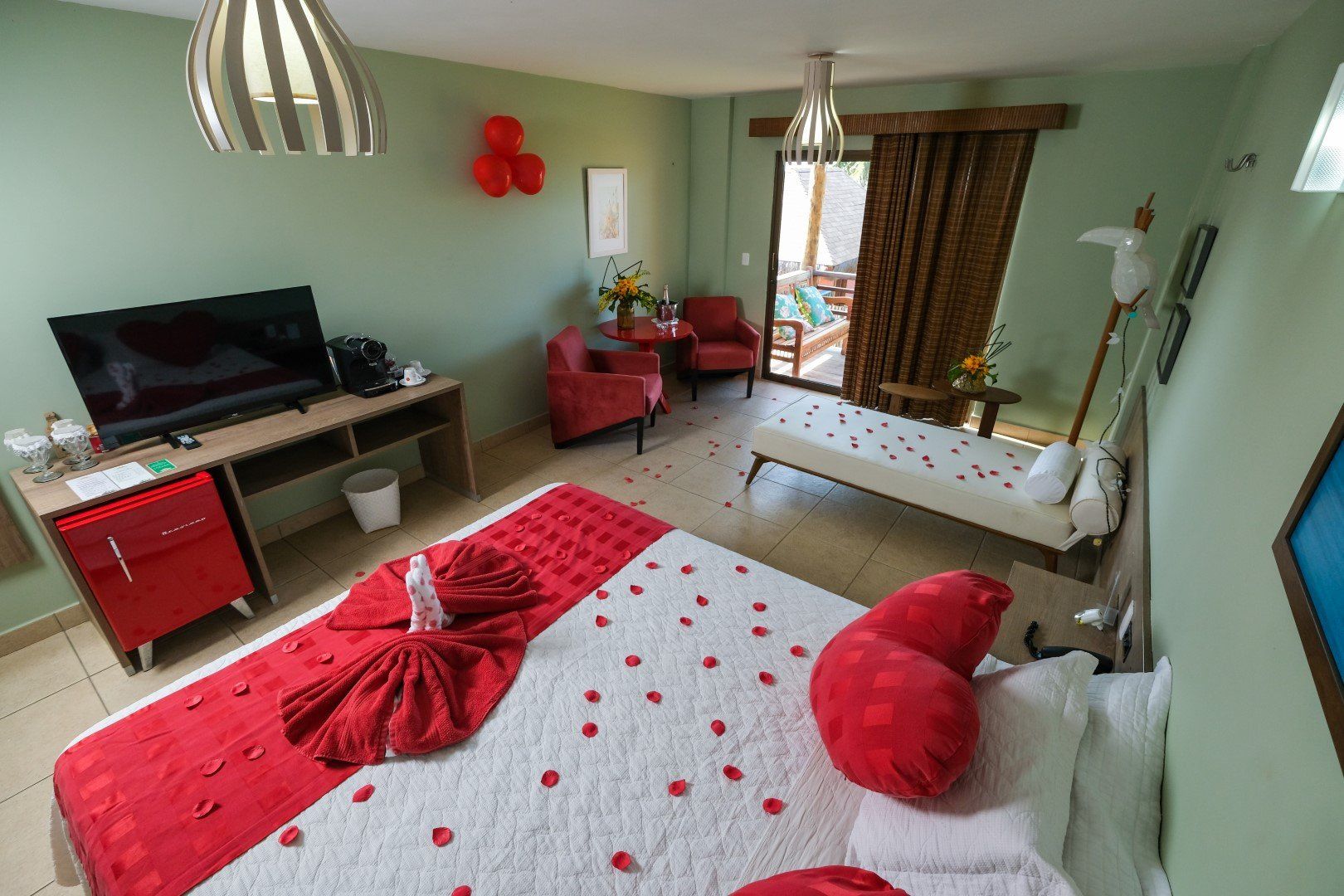 Um quarto de hotel com uma cama, televisão, cadeiras e balões.