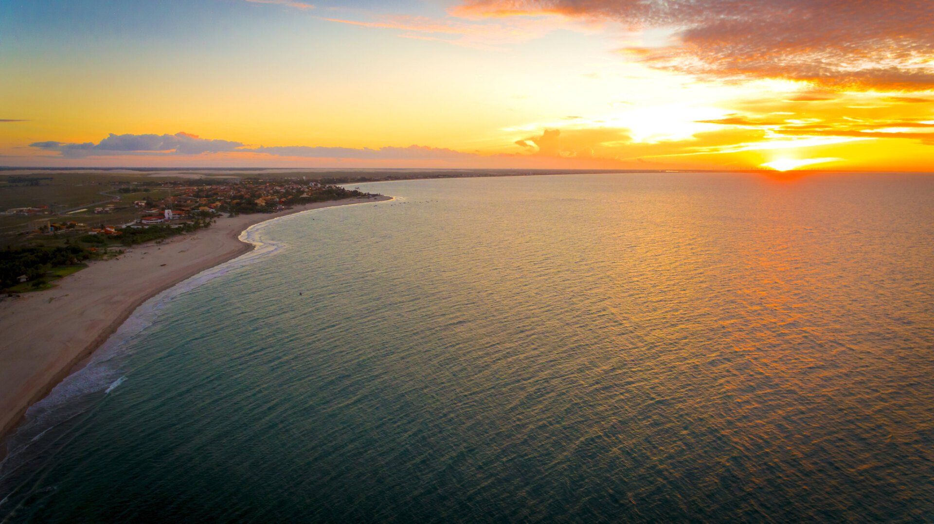 Uma vista aérea de uma praia e do oceano ao pôr do sol.