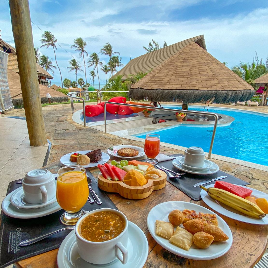 Uma mesa com pratos de comida e bebidas em frente a uma piscina.