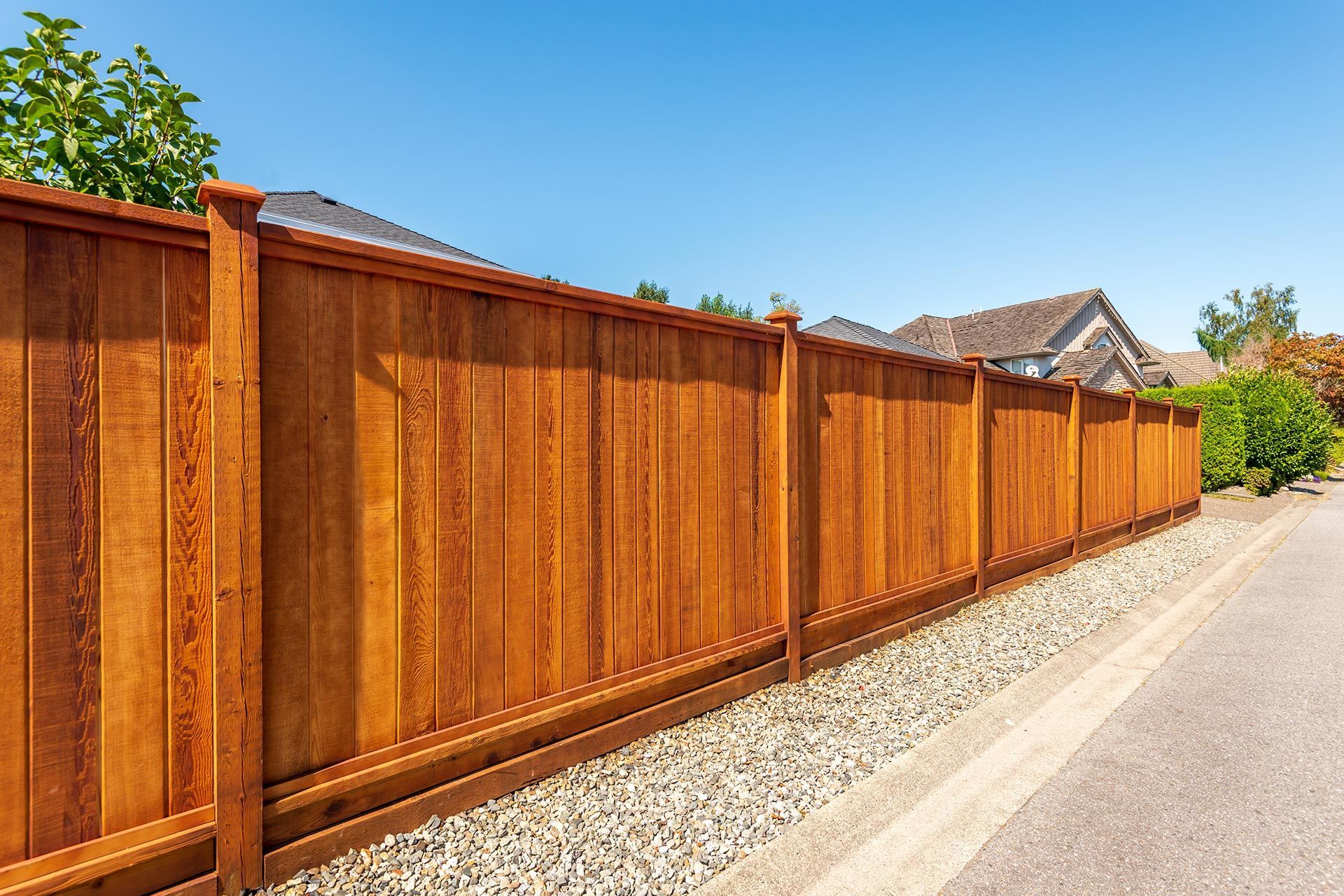 Wooden privacy fence along a paved road, gravel bed, blue sky. Wooden privacy fence along a paved road, gravel bed, blue sky.