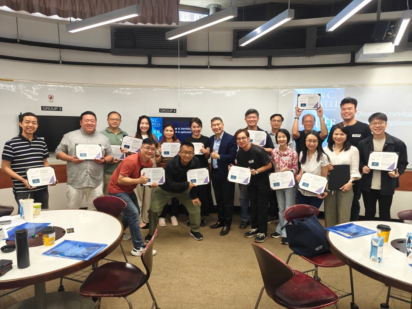 Group of people holding certificates, smiling in a classroom setting.