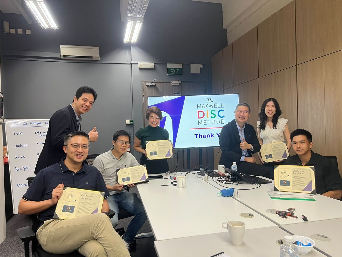 Group seated in a conference room holding certificates beside a “DISC” presentation screen.