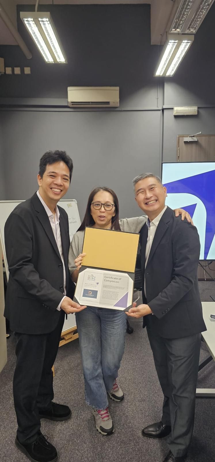 Three people at an indoor event hold a framed certificate and pose for a photo.