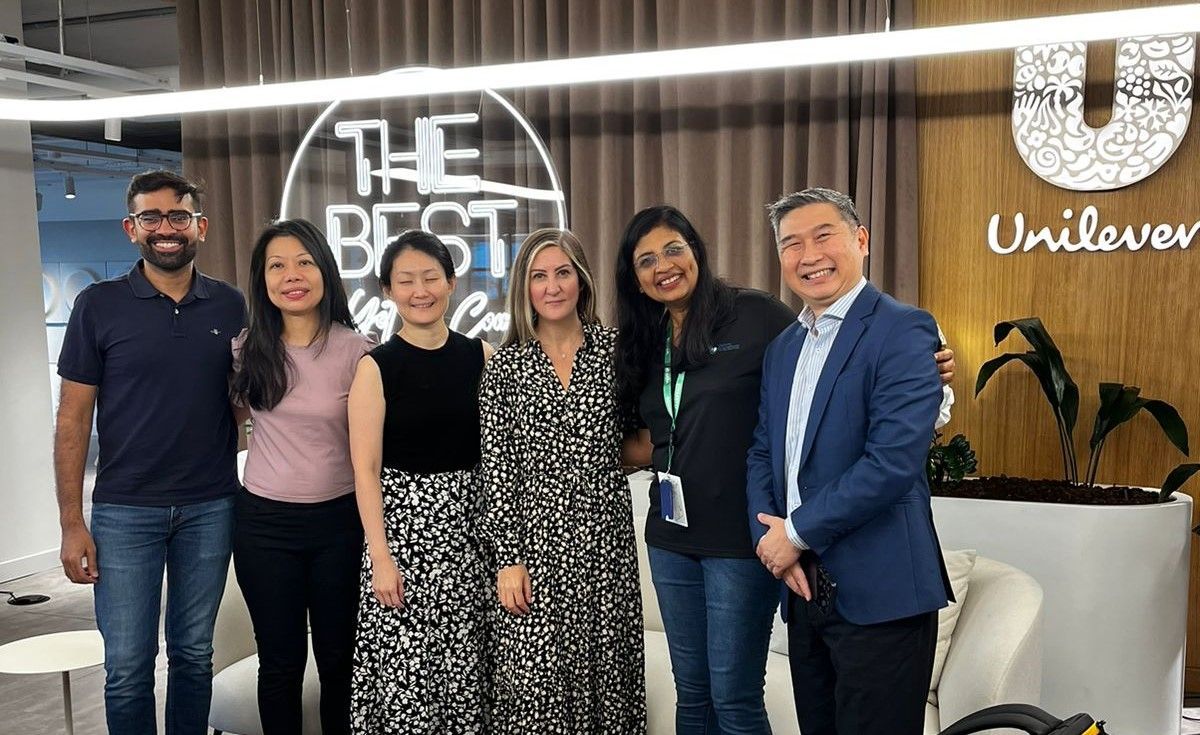 Six people pose in front of a Unilever logo. 