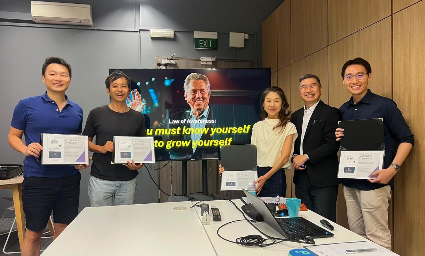 Six people posing in a conference room, holding certificates in front of a presentation screen.