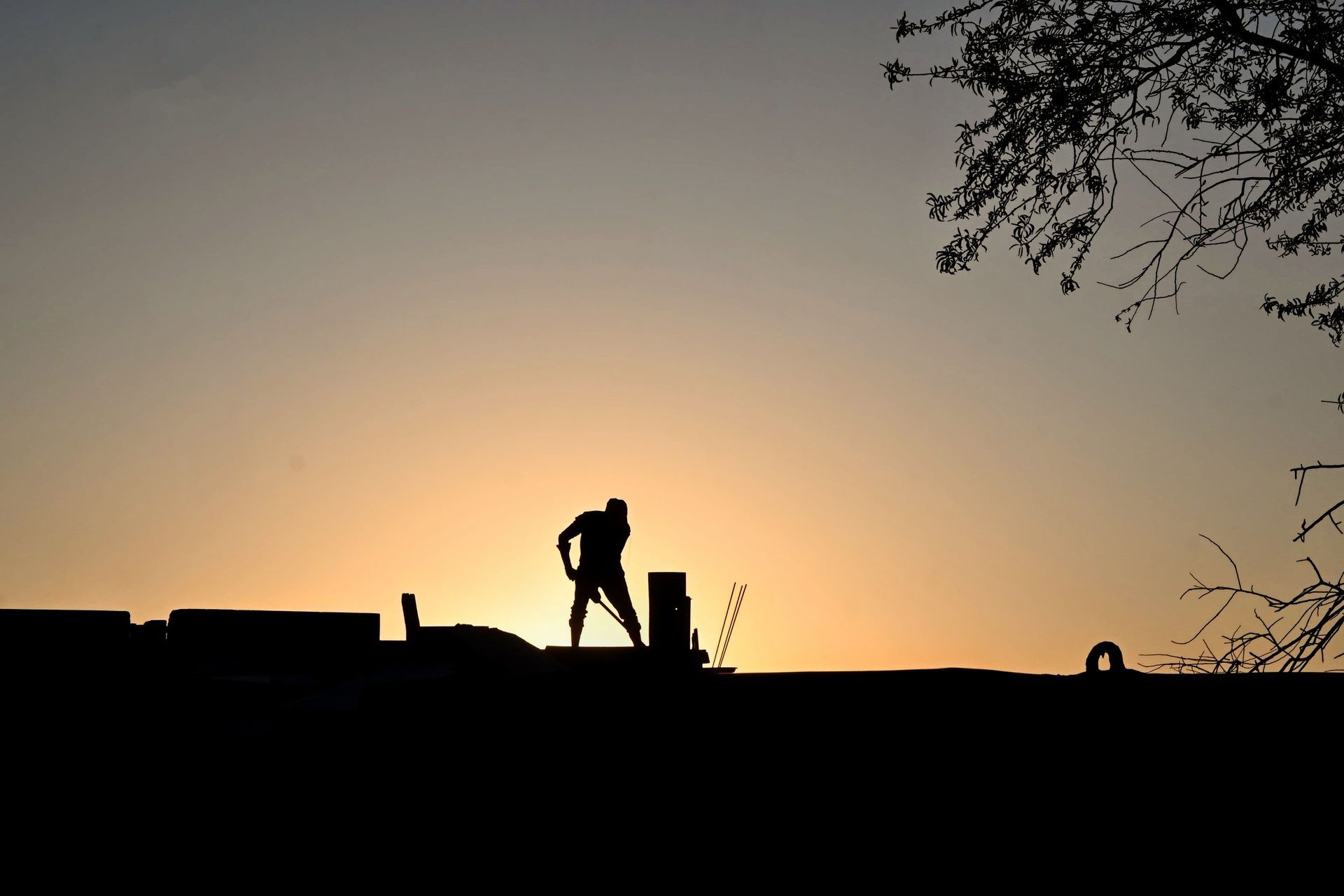 Silhouette of a worker on a rooftop at sunset, with a warm orange sky behind.