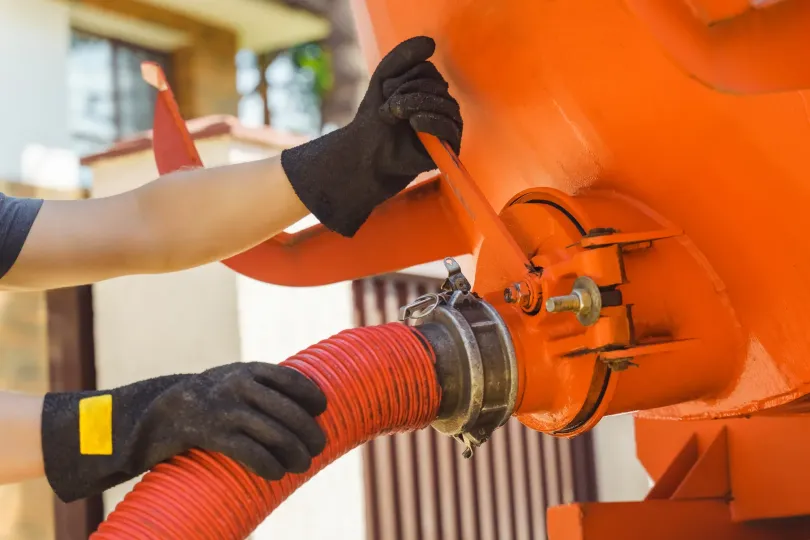 Gloved hands attach a red hose to an orange industrial machine.