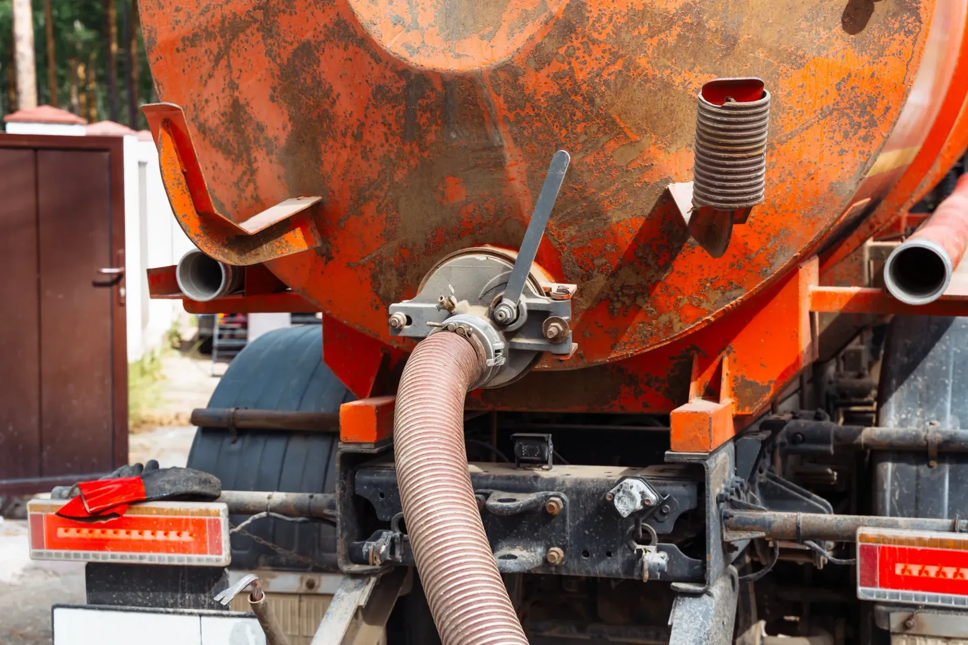 Orange cement mixer truck rear with hose and chute, splattered with dried concrete and rust patches