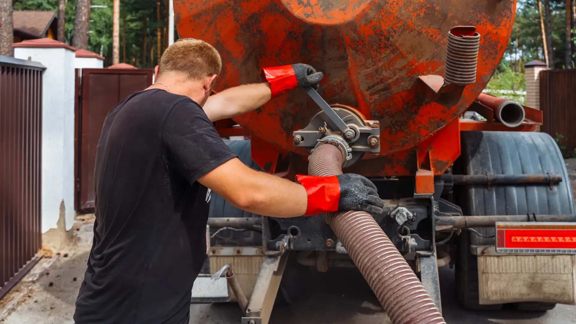 Worker vacuuming debris from the back of a red truck outdoors