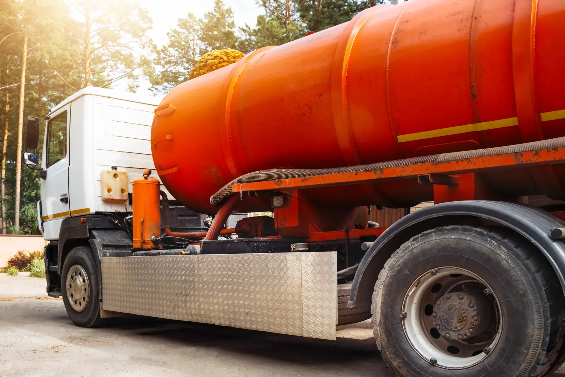 Orange tanker truck on a road, side view with silver cab and tank body