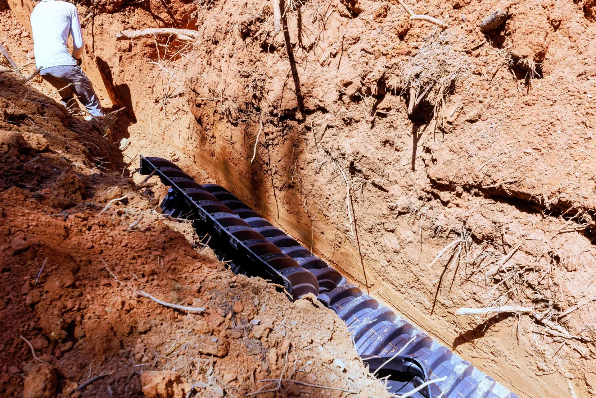 Workers laying a black pipe in a dirt trench