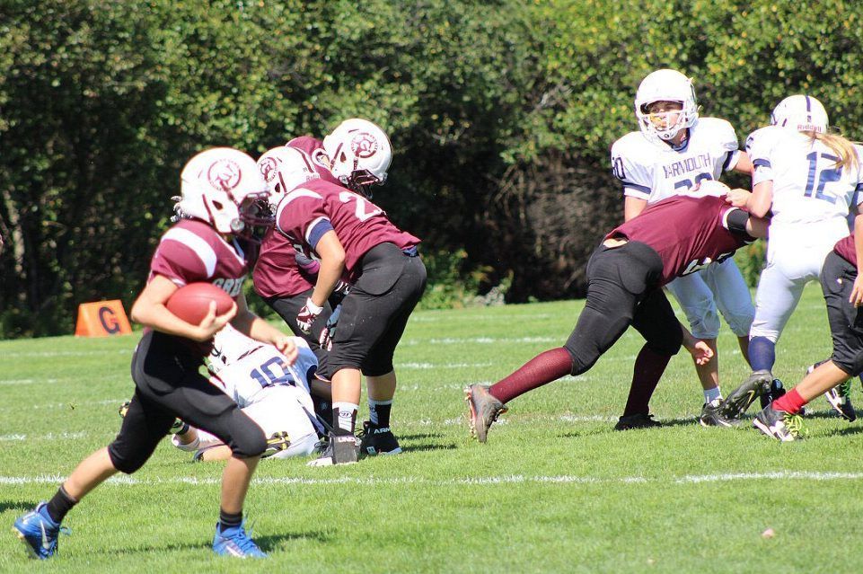High school football players in maroon and white tackle on a grassy field