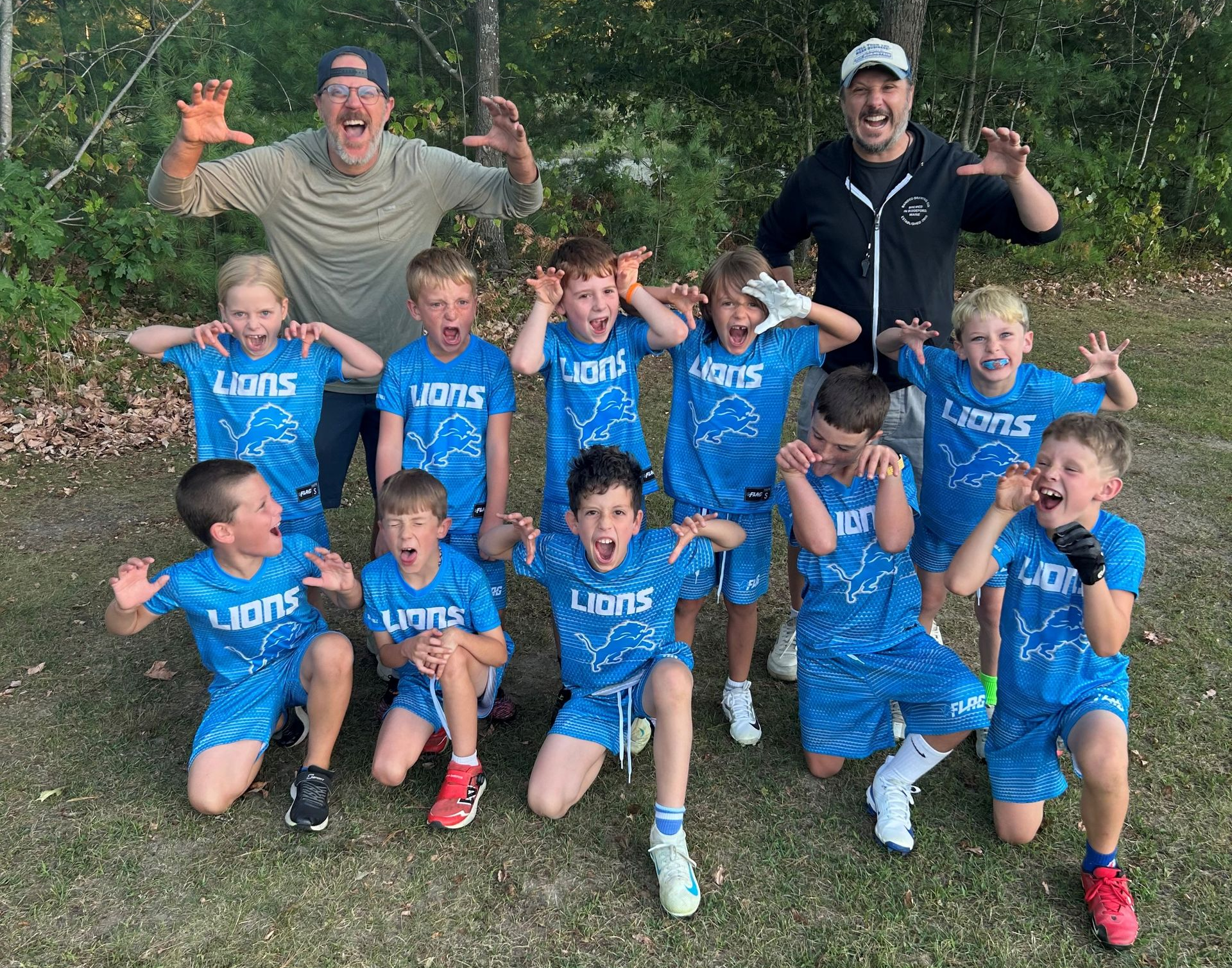 Youth soccer team and coaches posing outdoors, smiling and flexing in blue uniforms.
