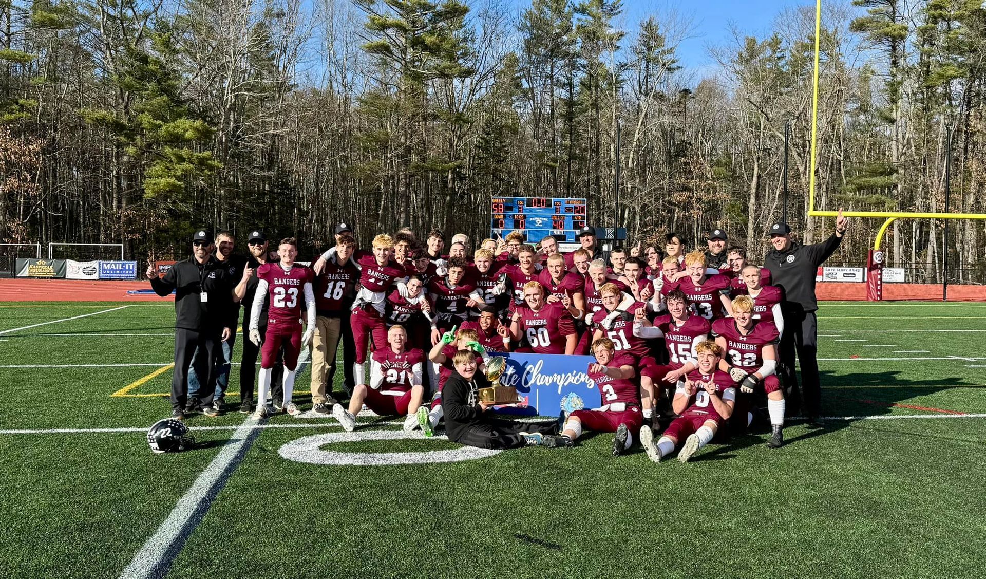 Football team posing on a field in maroon uniforms with a blue championship banner.