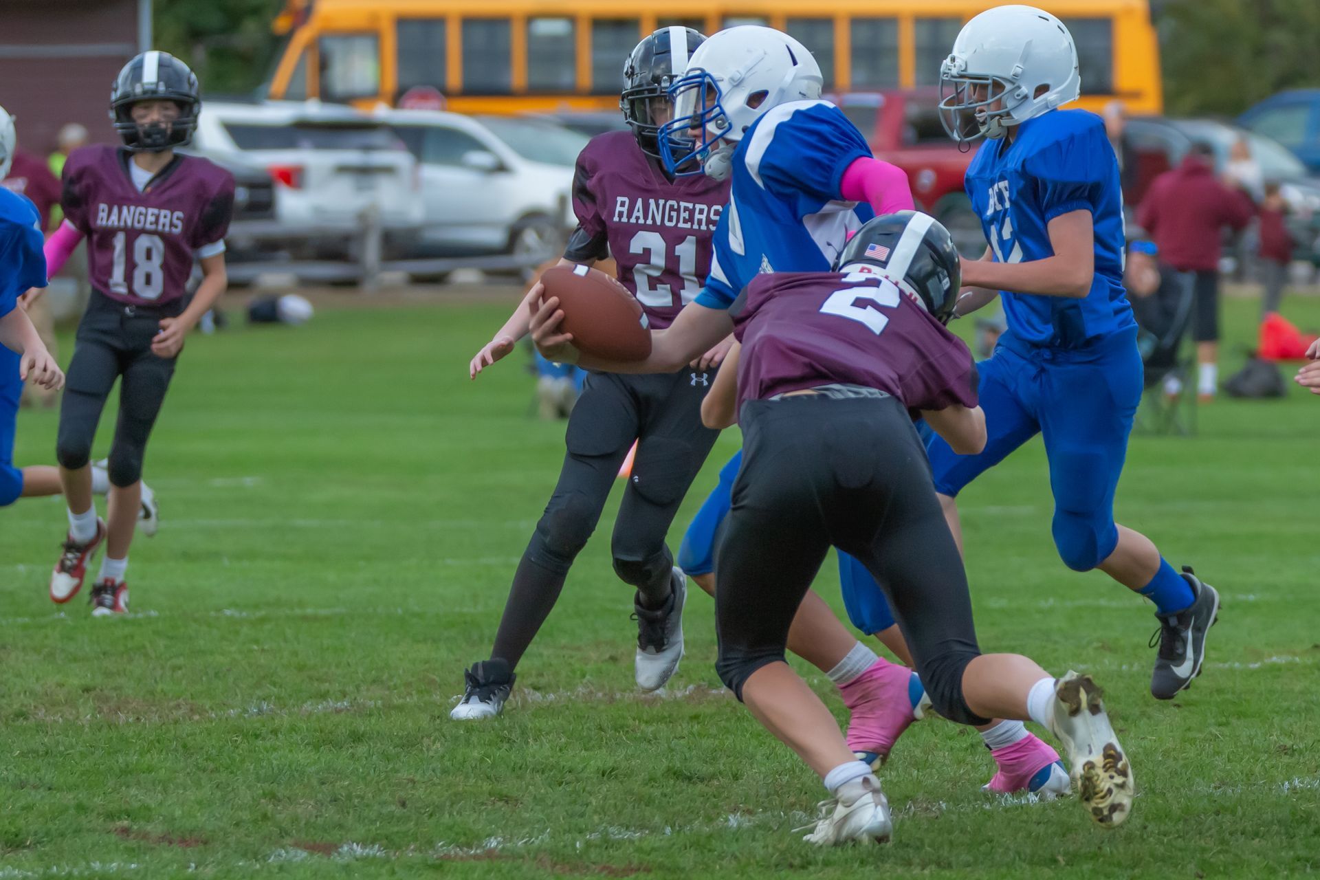 Youth football players in maroon and blue collide on a wet field during a game