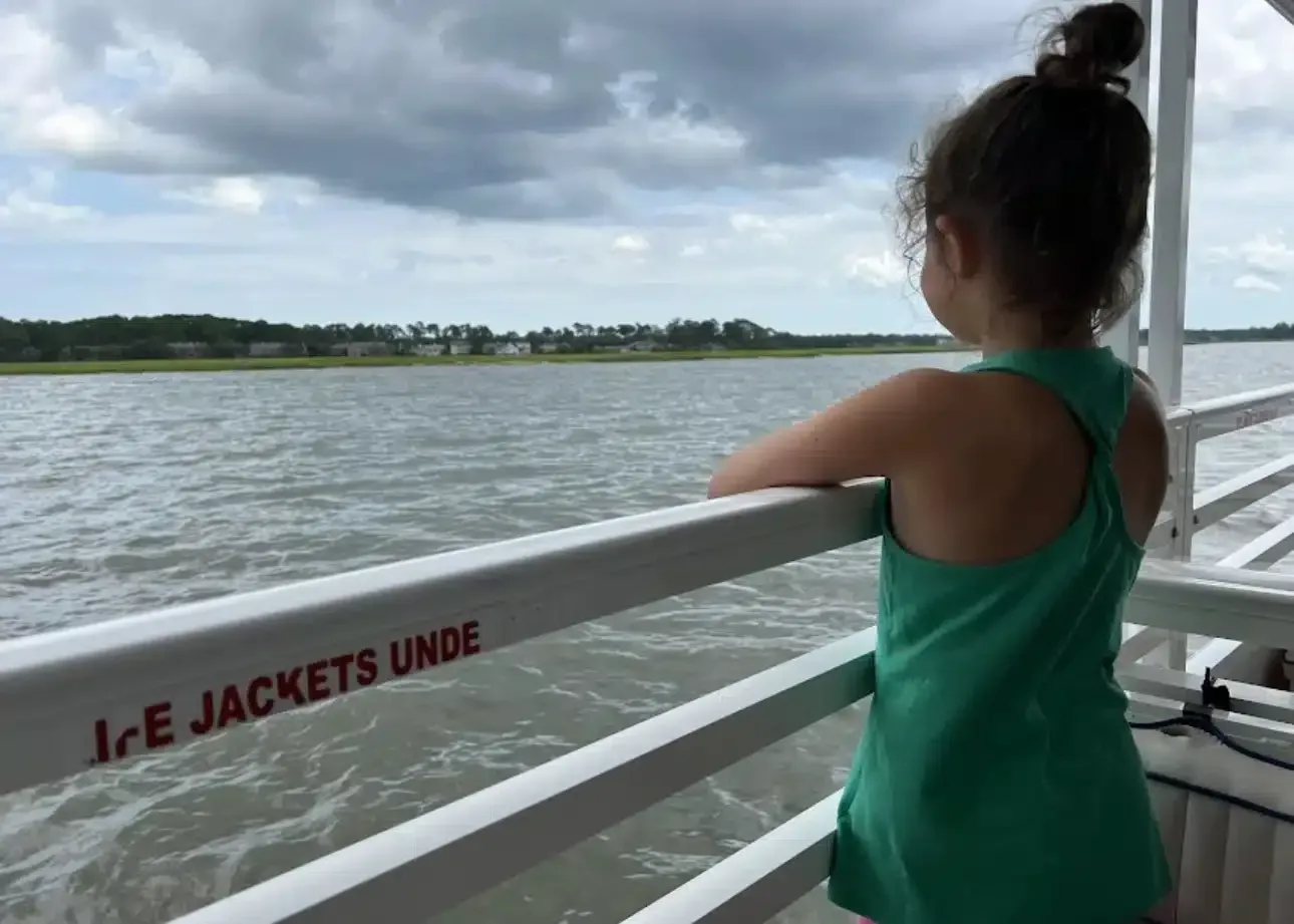 A little girl is standing on a boat looking at the water.