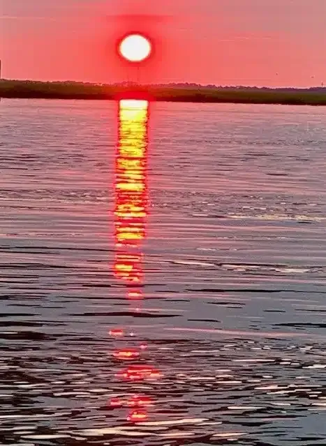 A sunset over a body of water with the sun reflected in the water.