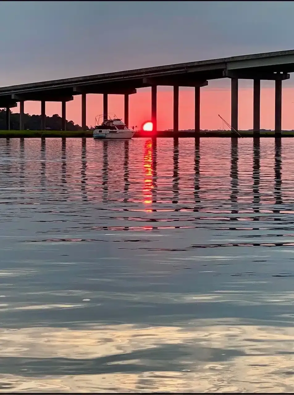The sun is setting behind a bridge over a body of water