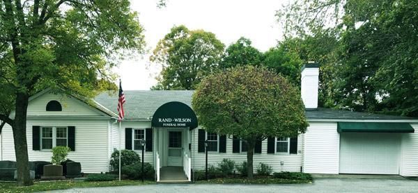 White building with a green awning. American flag on the left. Trees surround the building.