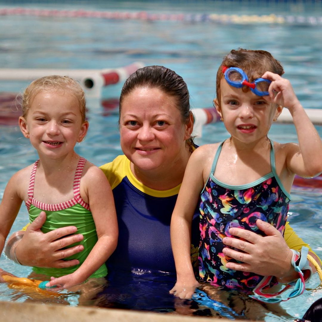 A woman is holding two little girls in a swimming pool