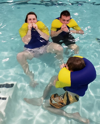 Three people are in a swimming pool wearing life jackets
