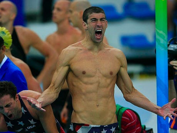 A shirtless swimmer with his arms outstretched is wearing usa swim trunks