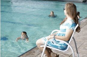 A woman is sitting in a chair next to a swimming pool watching a child swim.