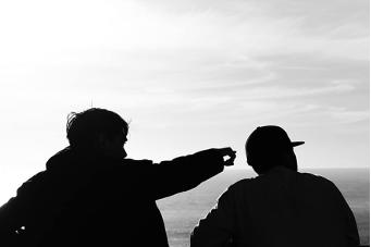 Two people are sitting next to each other and one is pointing at something.