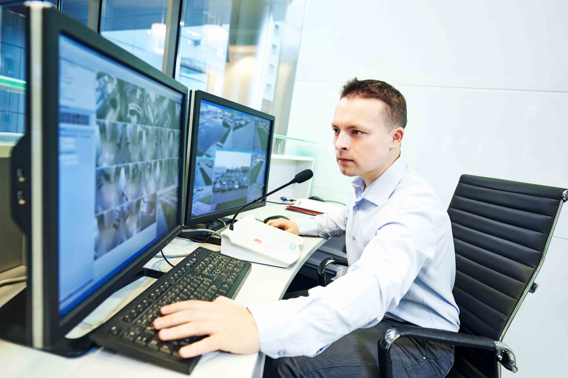 Two people monitoring screens in a security control room. Large wall display shows surveillance feeds.
