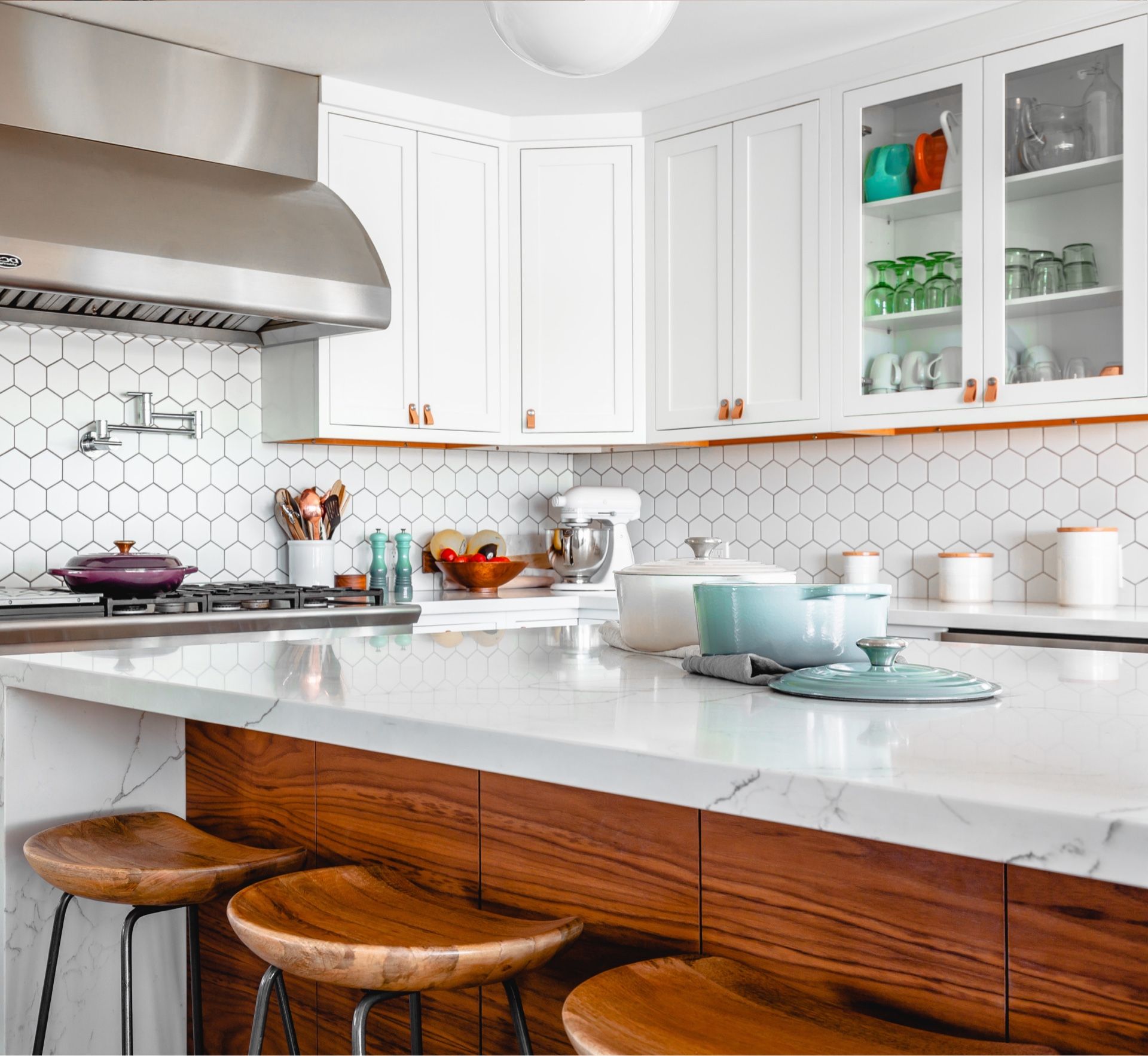 Cuisine moderne avec armoires blanches, touches de bois et comptoirs en marbre ; trois tabourets en bois à l'îlot central.