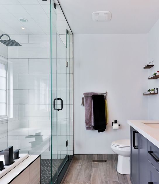 A modern bathroom with a glass-enclosed shower, wood-look tile flooring, gray cabinets, and towels hanging on the wall.