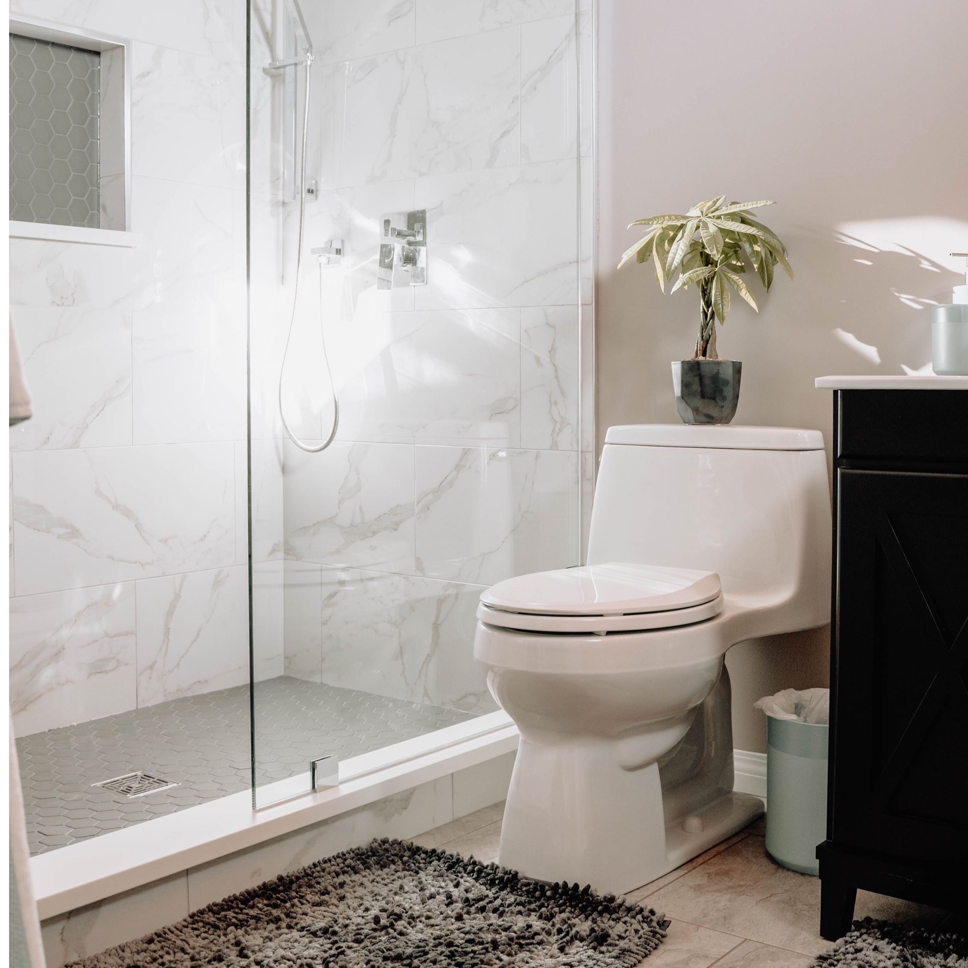 Modern bathroom with marble shower, white toilet, black cabinet, and rug.