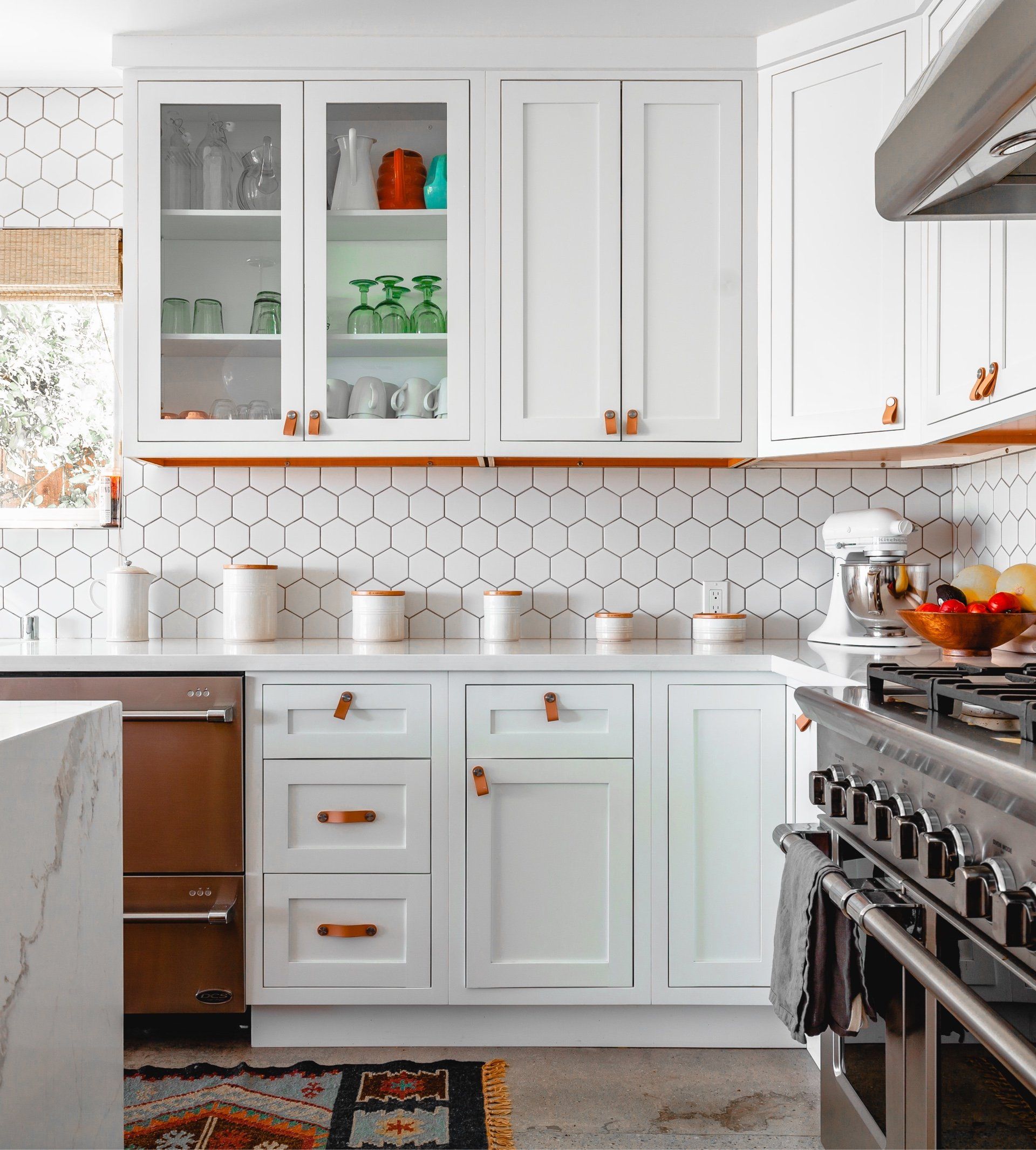 White kitchen with hexagonal tile backsplash and copper hardware.