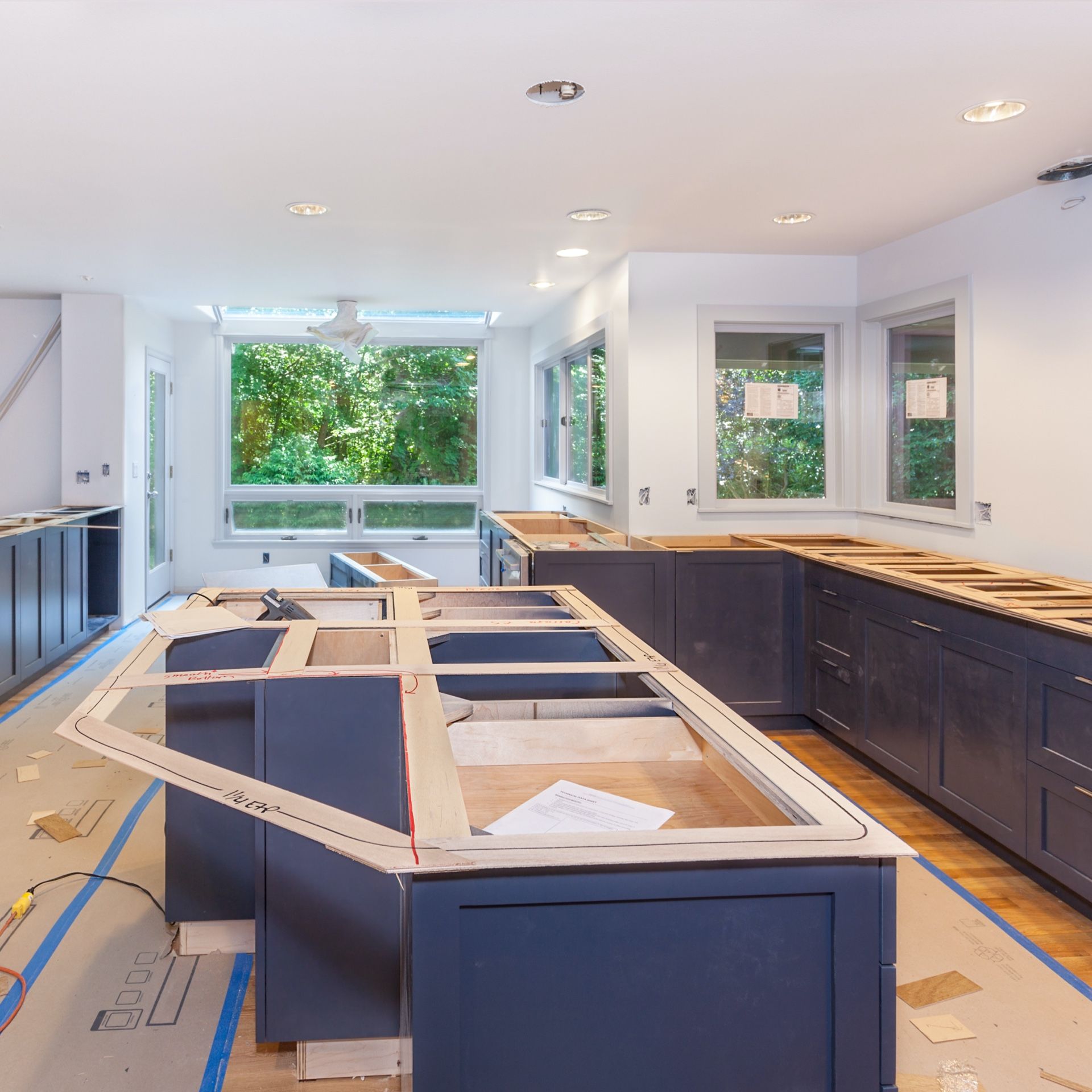 Kitchen renovation in progress, featuring dark blue cabinets, unfinished island, and large windows.