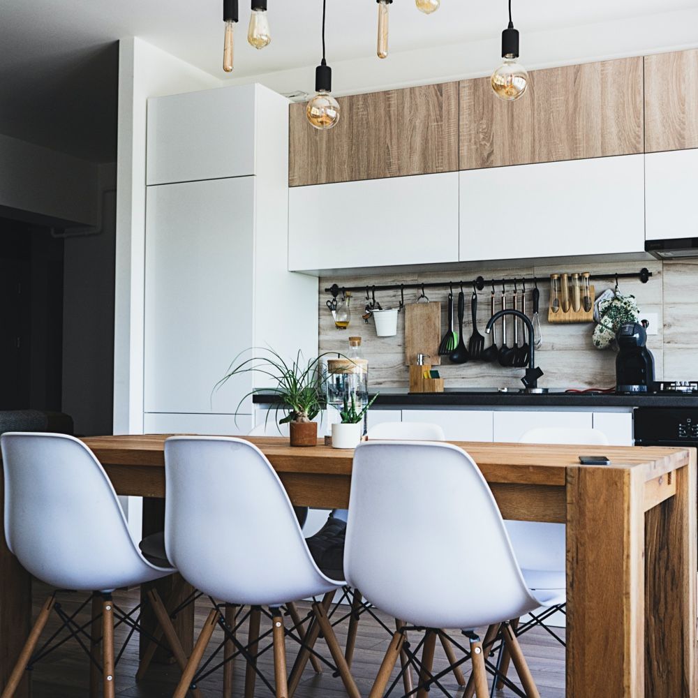 Modern kitchen with white cabinets, wooden table and chairs, and decorative light fixtures.