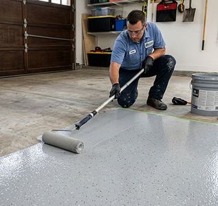 Person rolling gray epoxy coating onto a garage floor with a paint roller