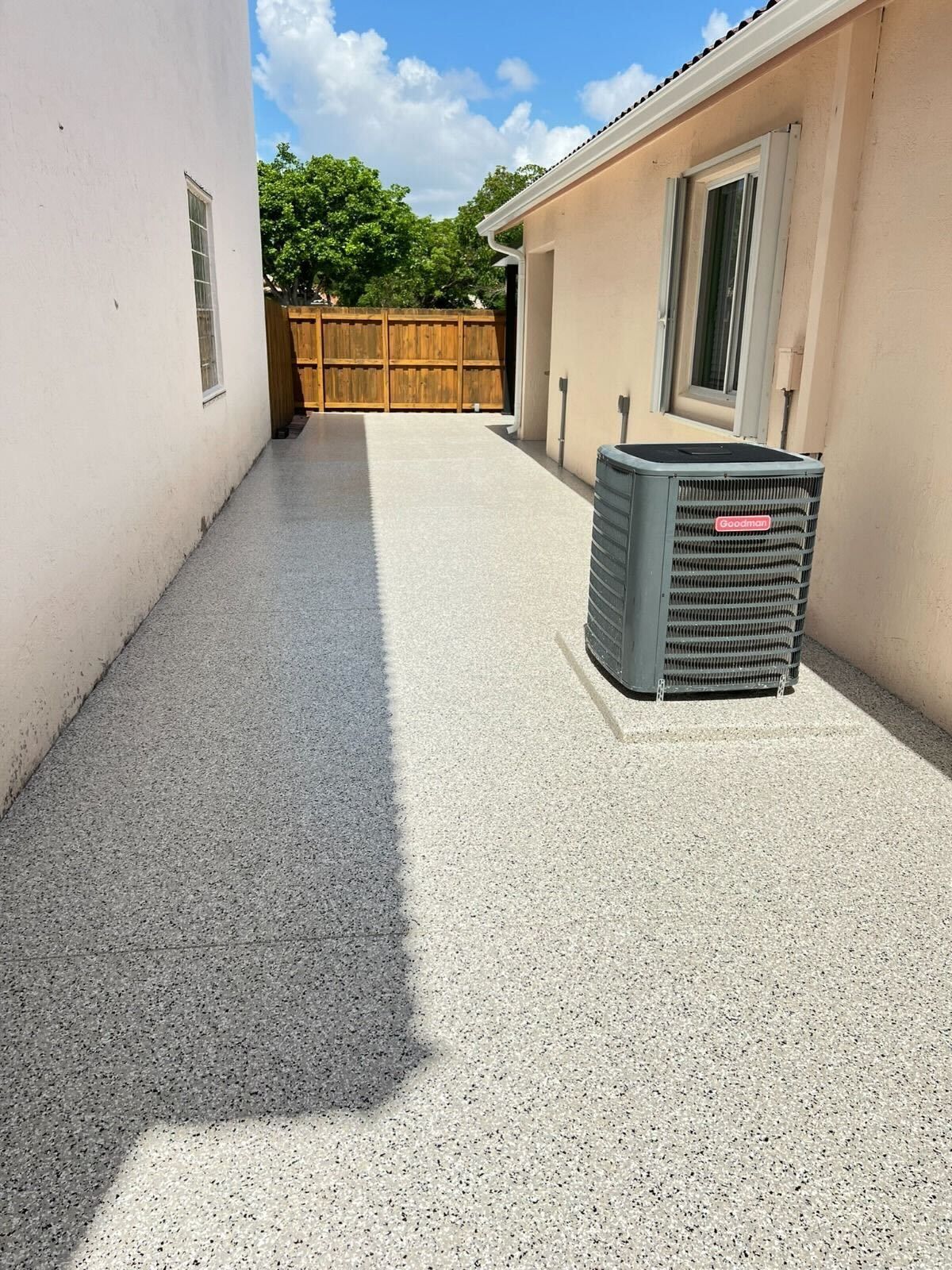 Narrow concrete side yard between houses with a wooden gate and an air conditioner unit beside the wall.