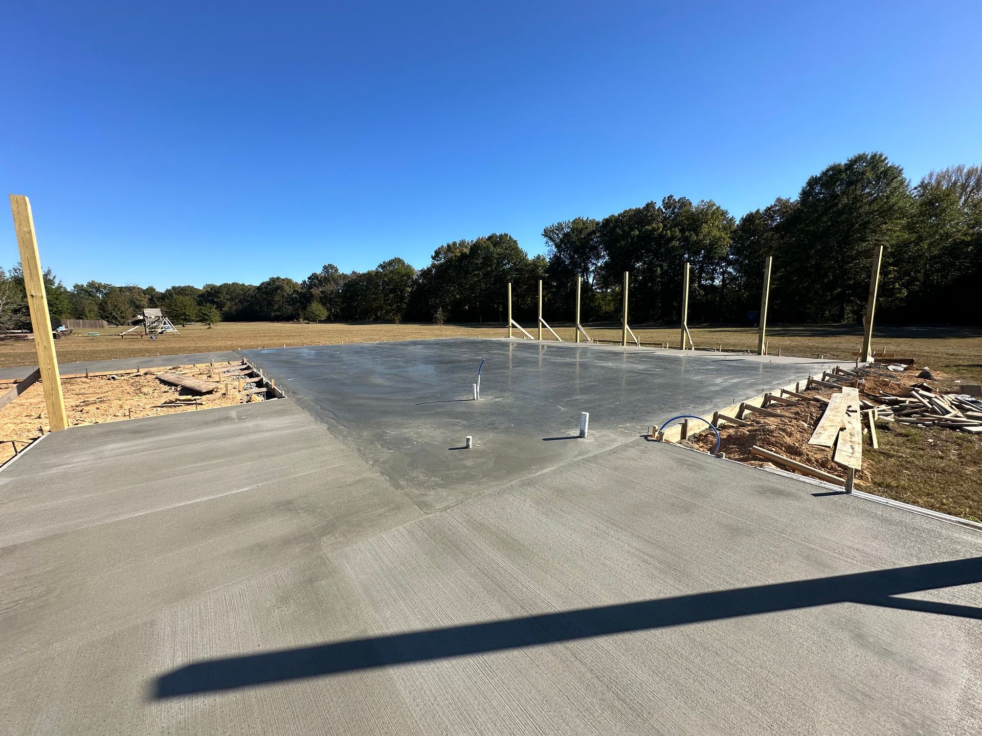 Freshly paved road at a construction site with dirt shoulders and trees under a clear blue sky