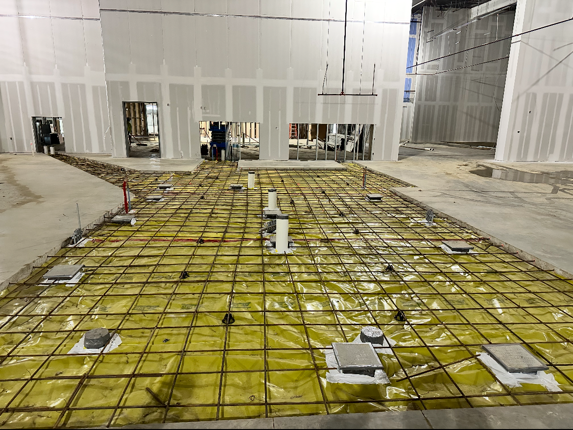 Construction site with yellow waterproofing membrane and rebar grid in a large unfinished interior