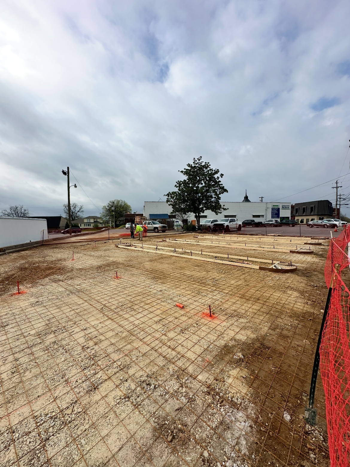 Construction site with rebar foundation, orange safety netting, and cloudy sky.