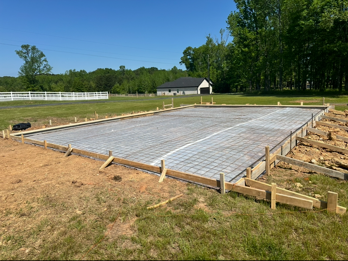 Concrete foundation slab with rebar and wooden forms at a rural construction site under a blue sky